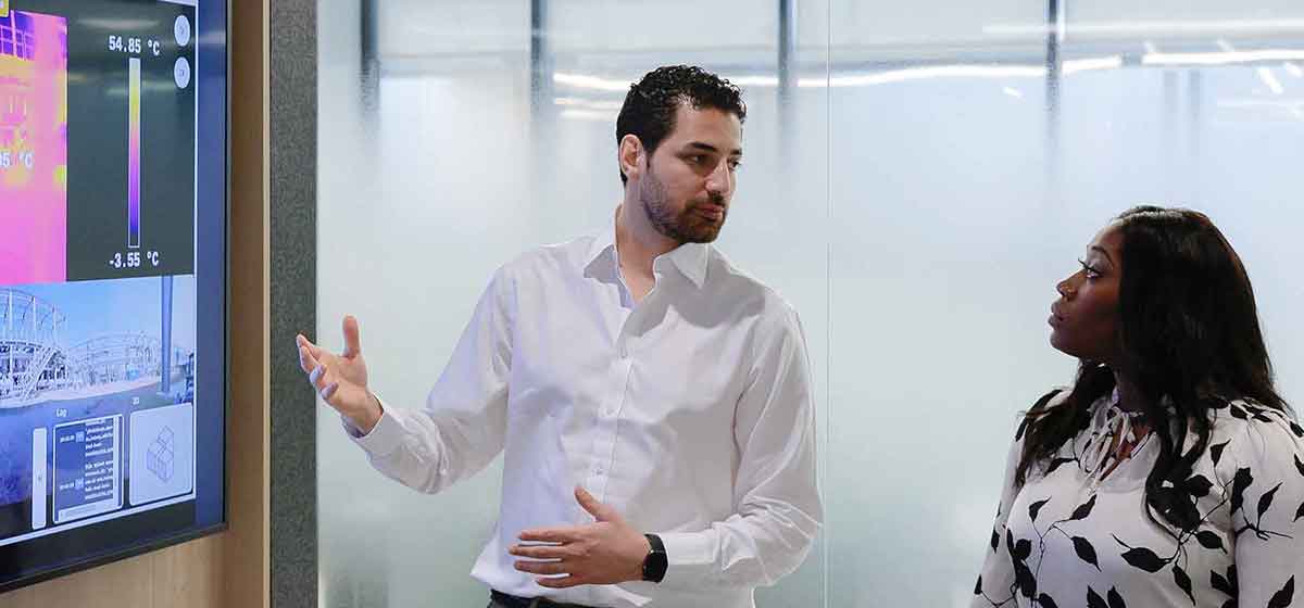 Photo of 2 SLB employees discussing results from OptiSite facility, equipment, and pipeline solutions.