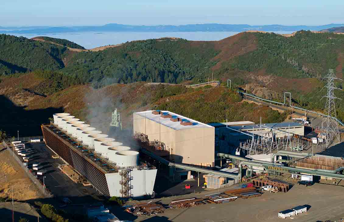 Photograph of steam issuing from a geothermal power plant in hilly terrain.