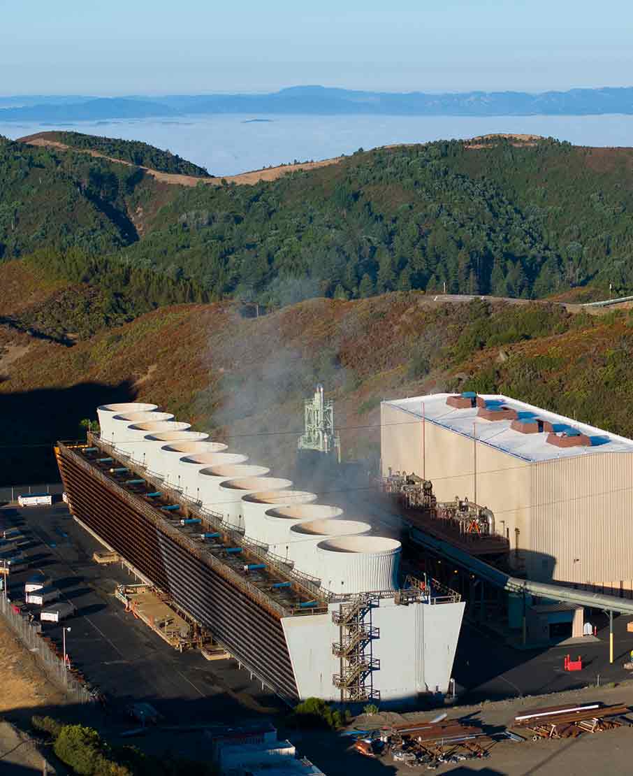 Photograph of steam issuing from a geothermal power plant in hilly terrain.