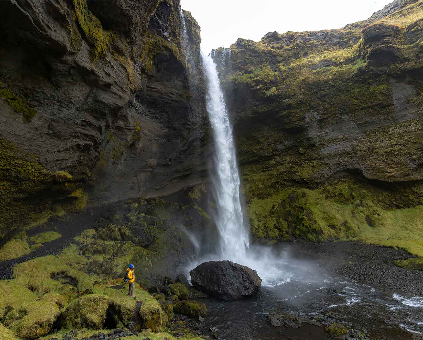 A person far in the distance looking up at a waterfall