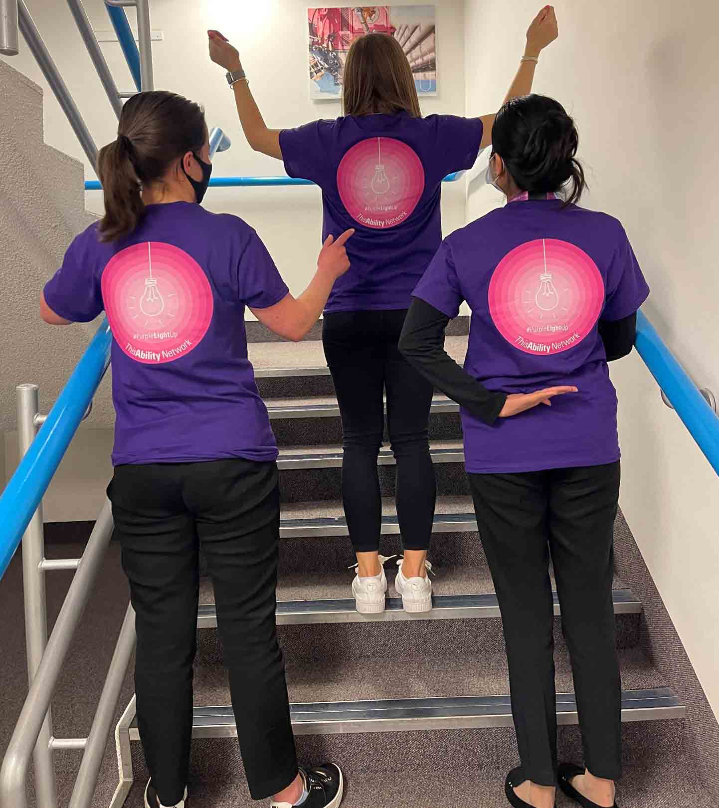 Three women celebrating disability day while showing support through wearing a purple t-shirt