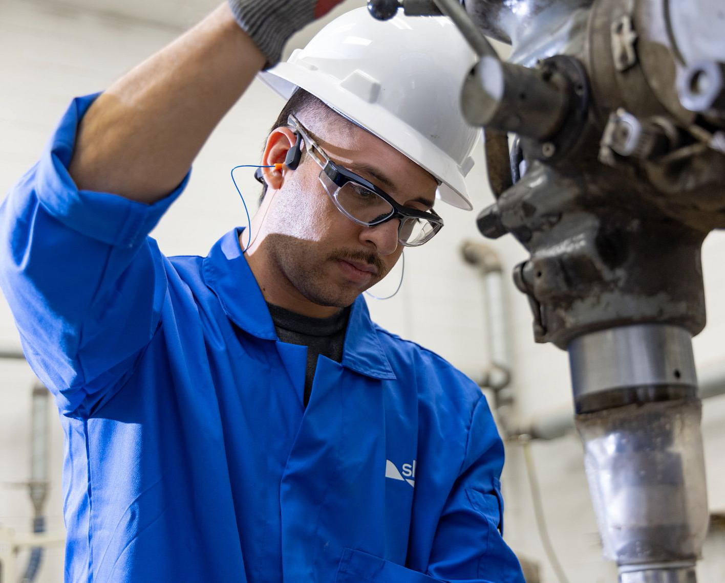 man in blue overalls and white hard hat using drill