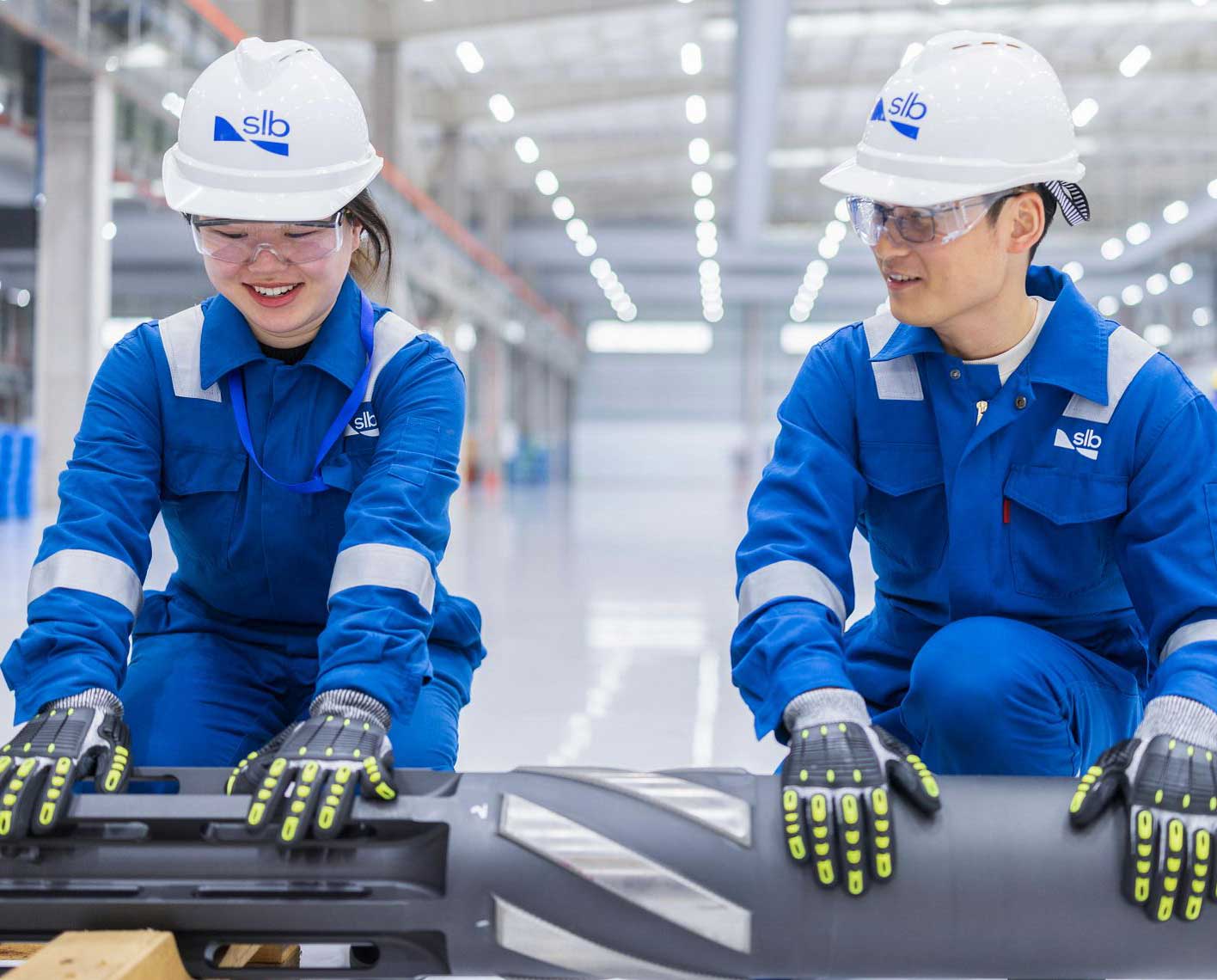 Two workers in safety gear handling a large component in a factory.