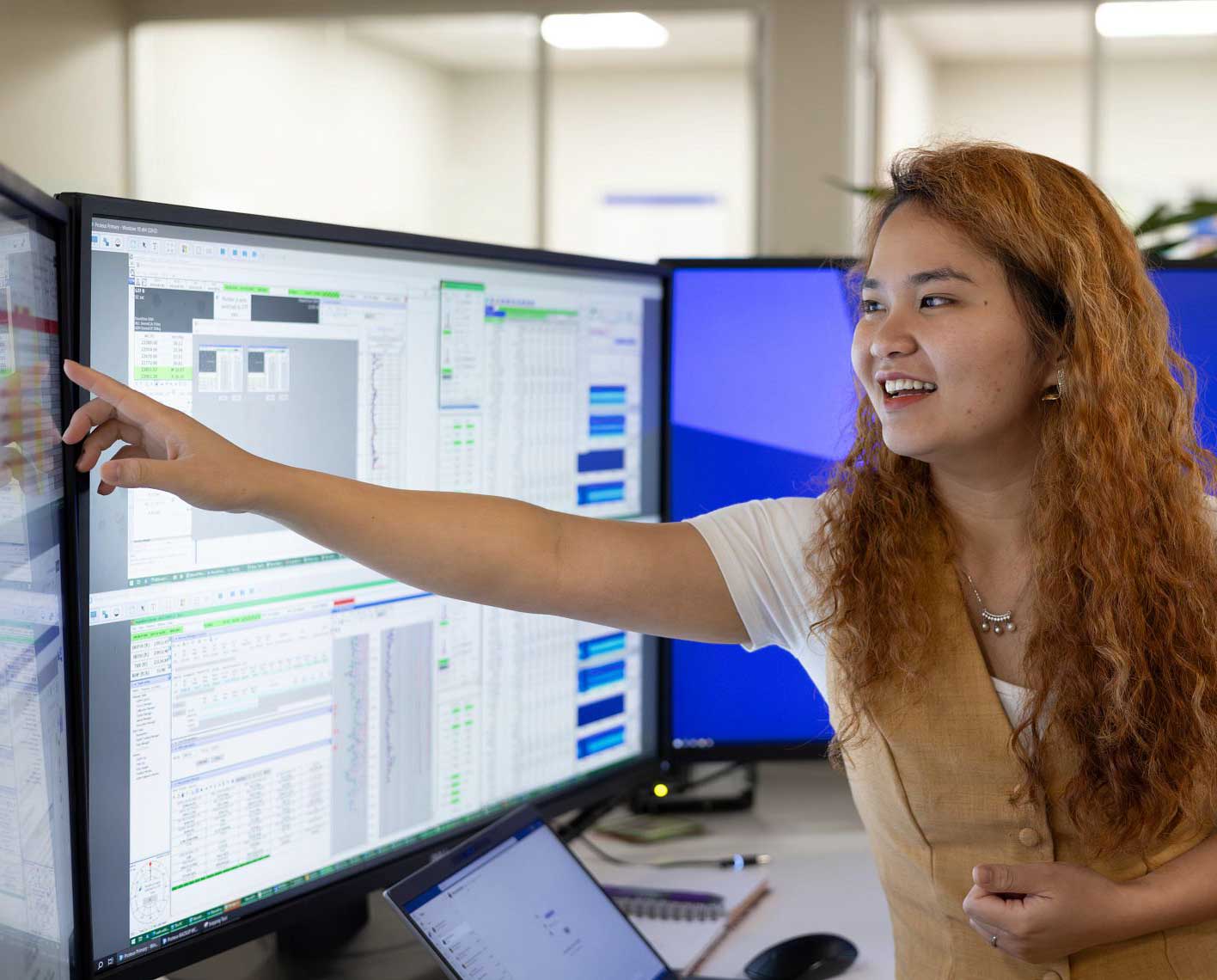 Girl pointing at data on three desktop monitors