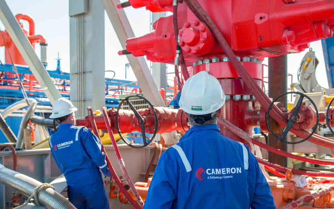 Two Cameron employees standing in front of red BOP on land rig.