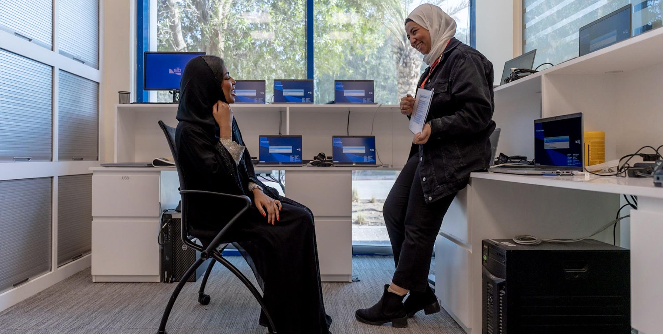 Two women sitting at a desk with laptops open