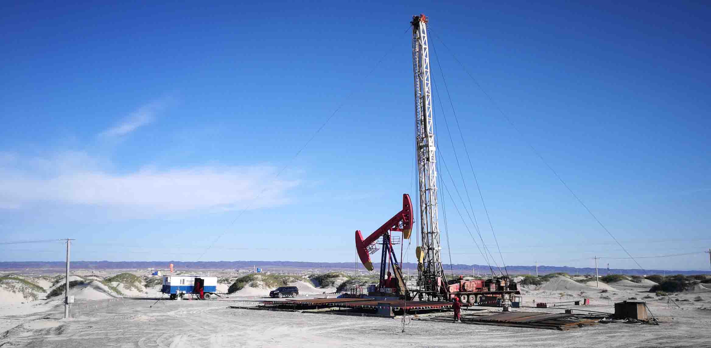 Photo of a workover rig and a nearby pumpjack in a barren area of remote northwest China. 