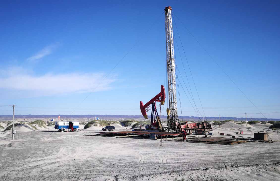 Photo of a workover rig and a nearby pumpjack in a barren area of remote northwest China.
