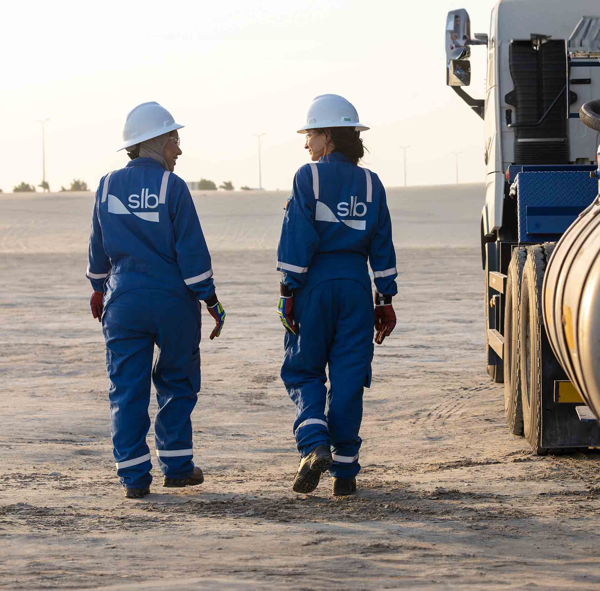 Two women walking next to a completions equipment truck in the desert