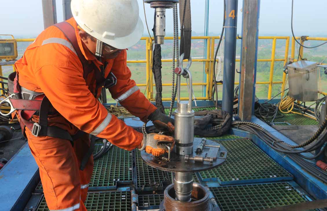 Photo of an SLB specialist on the tower, guiding an expandable steel patch into a well.
