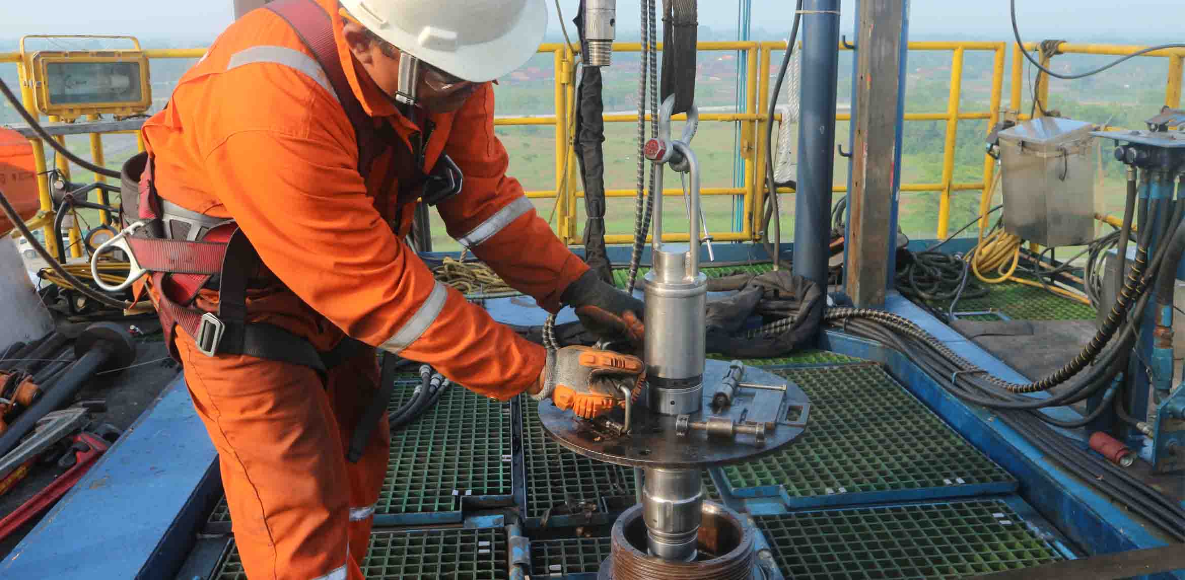 Photo of an SLB specialist on the tower, guiding an expandable steel patch into a well.  