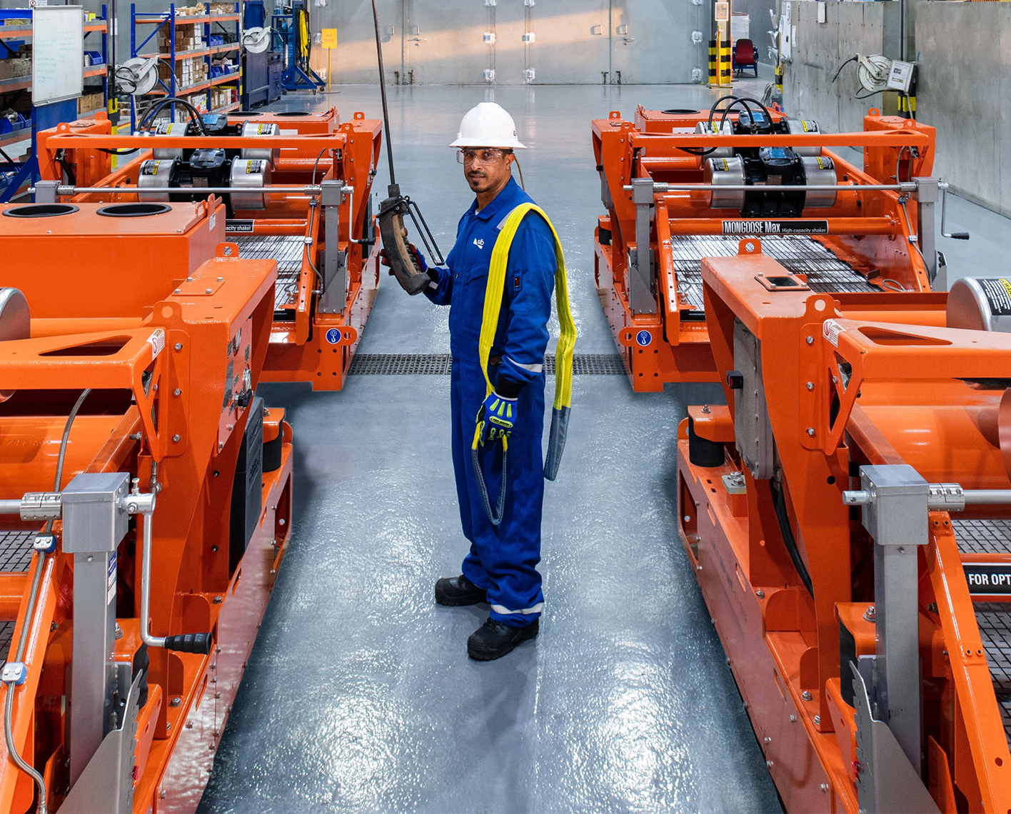 Factory worker in safety gear standing between large orange industrial machines.