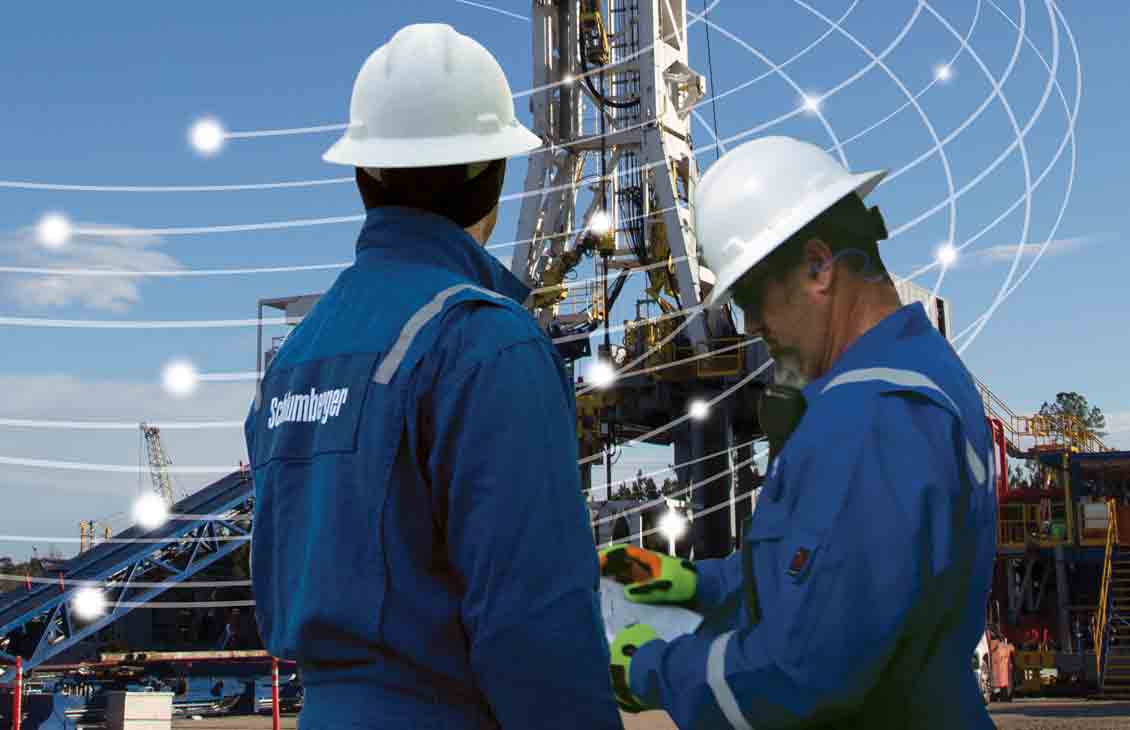 Schlumberger field workers look up at a rig.