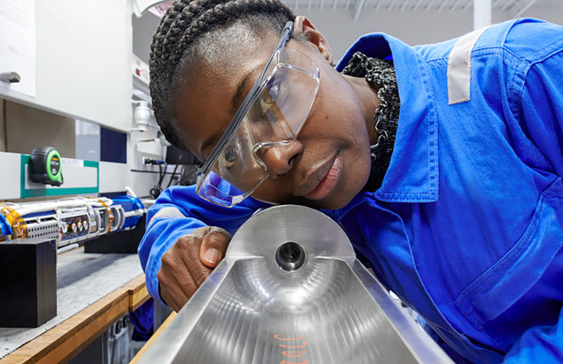 Photo of a woman but coveralls looking down an abandonment tool in a manufacturing facility (Tier 1_ManufacturingFacility_SugarLand_AML_5427)