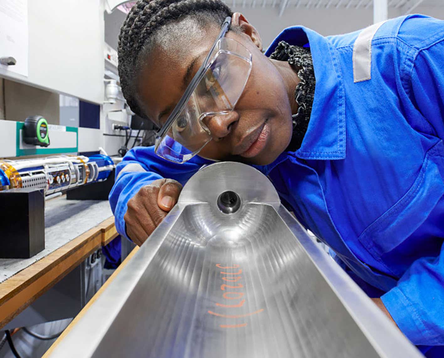 Photo of a woman but coveralls looking down an abandonment tool in a manufacturing facility (Tier 1_ManufacturingFacility_SugarLand_AML_5427)