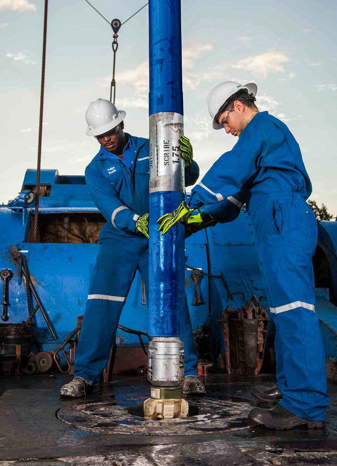 Two rig hands guide a clean BHA, including a PDC bit and drilling motor, down a well