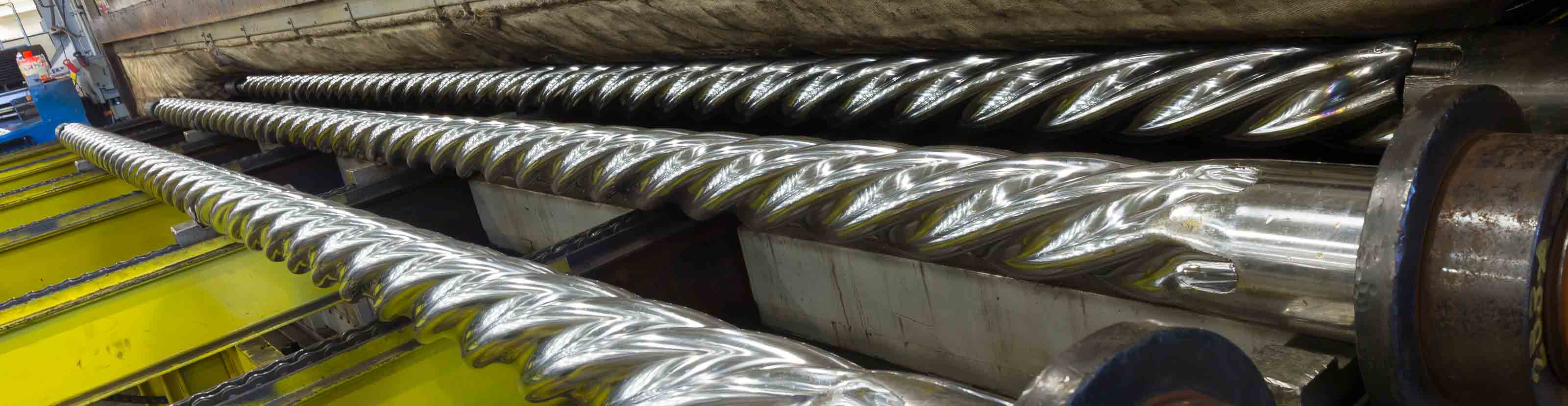 Three long, polished metal rotors on a rack, ready for assembly into drilling motors