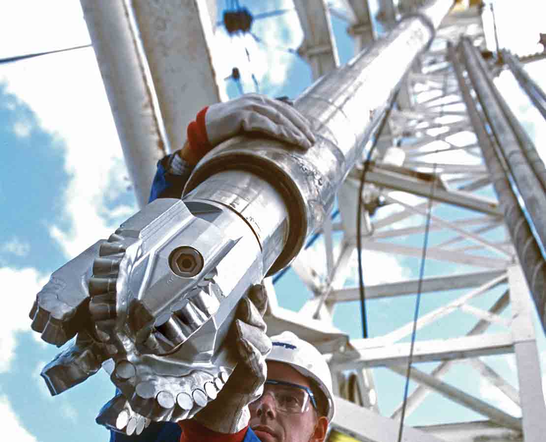 Looking up at a Schlumberger drilling technician guiding a brand-new PowerDrive Xceed ruggedized RSS and PDC bit into a well