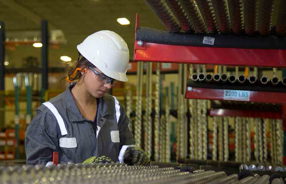 A manufacturing technician examining a rack holding dozens of small-diameter drilling motor rotors