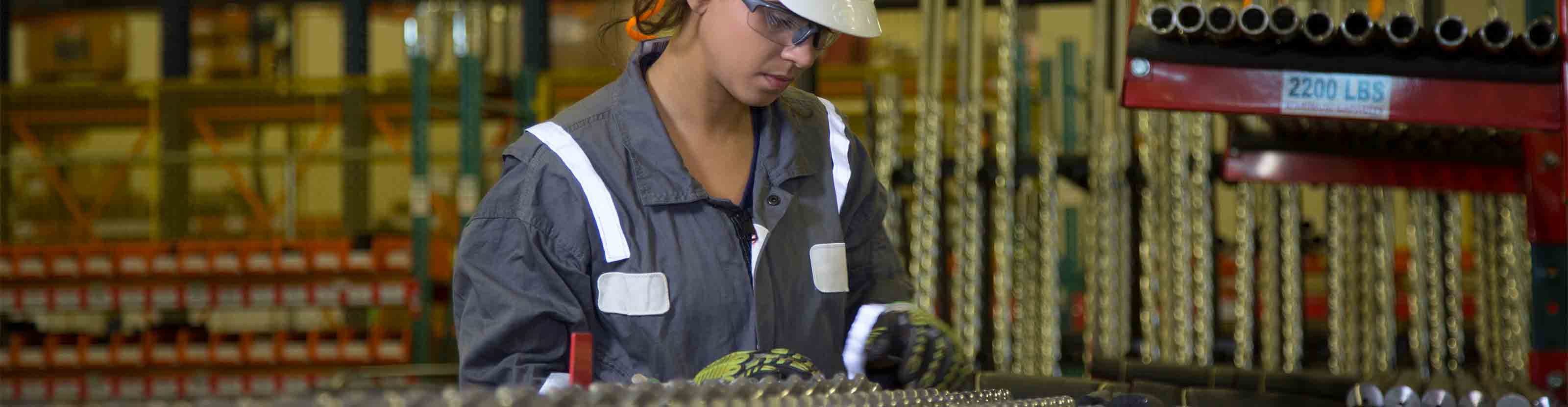 A manufacturing technician examining a rack holding dozens of small-diameter drilling motor rotors