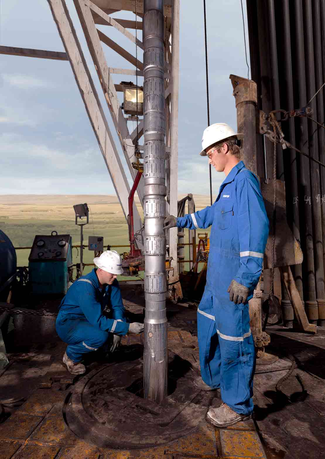 Two Schlumberger technicians adjust an LWD tool on a drilling rig floor