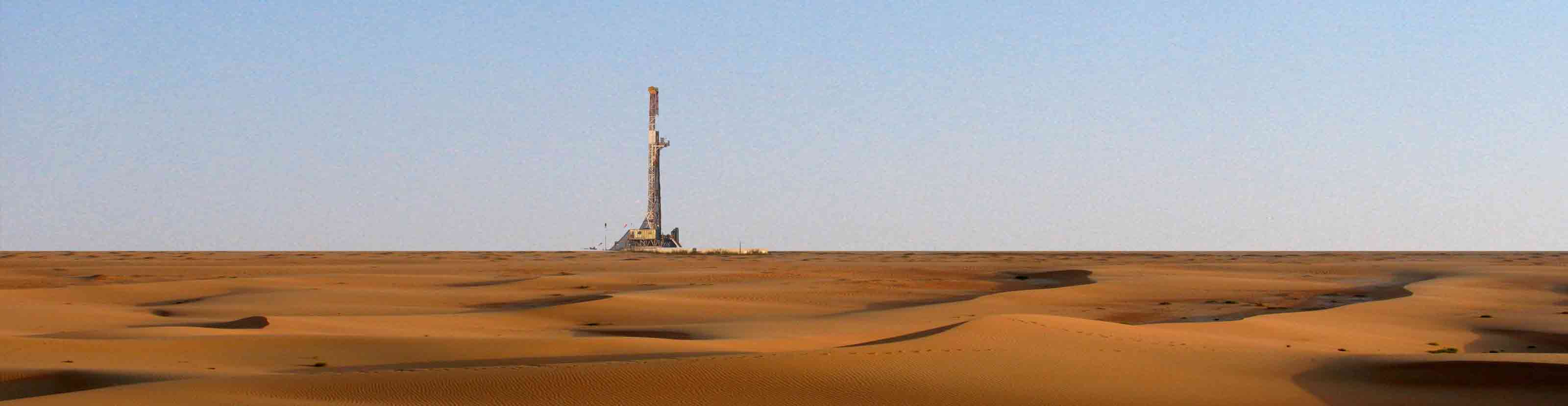 A land rig in the distance, across a sandy landscape
