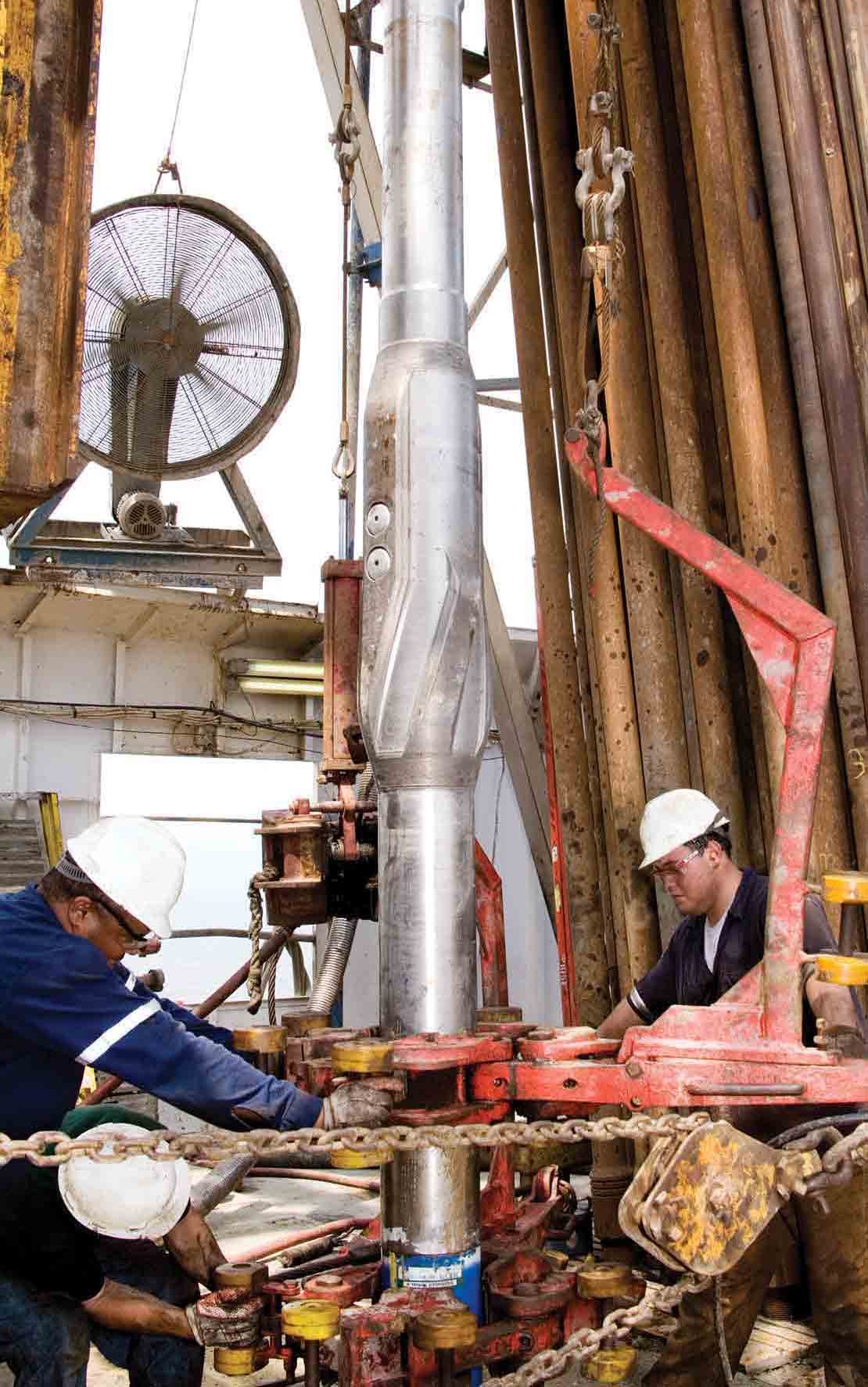 Three technicians preparing the StethoScope formation pressure-while-drilling service tool to go downhole with the aid of an iron roughneck