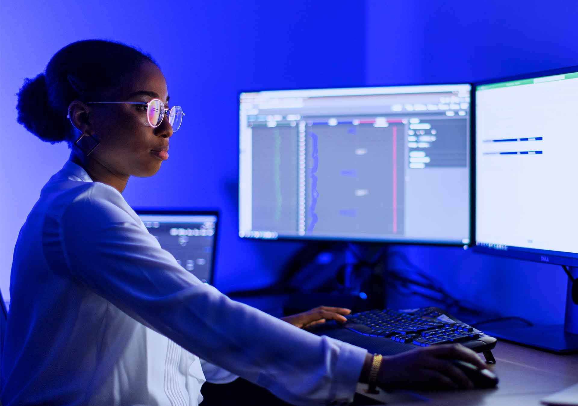 ): Engineer working on many screens at a desk in the Performance Live service center.