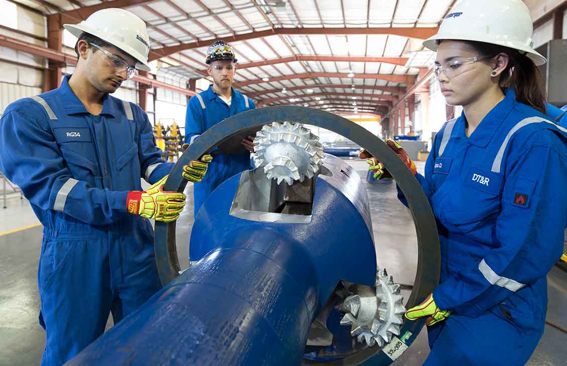 Three Schlumberger workers performing maintenance on a drilling-type underreamer.