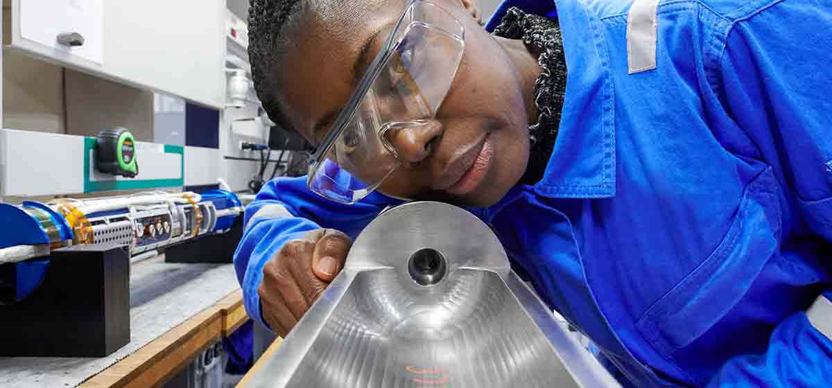 Photo of a woman but coveralls looking down an abandonment tool in a manufacturing facility (Tier 1_ManufacturingFacility_SugarLand_AML_5427)
