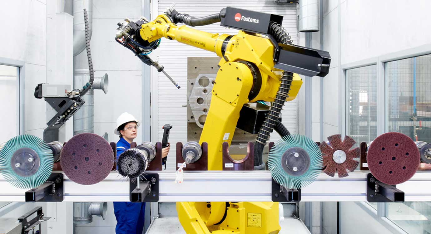 Employee in blue coveralls and white helmet using remote to guide a yellow inspection robot