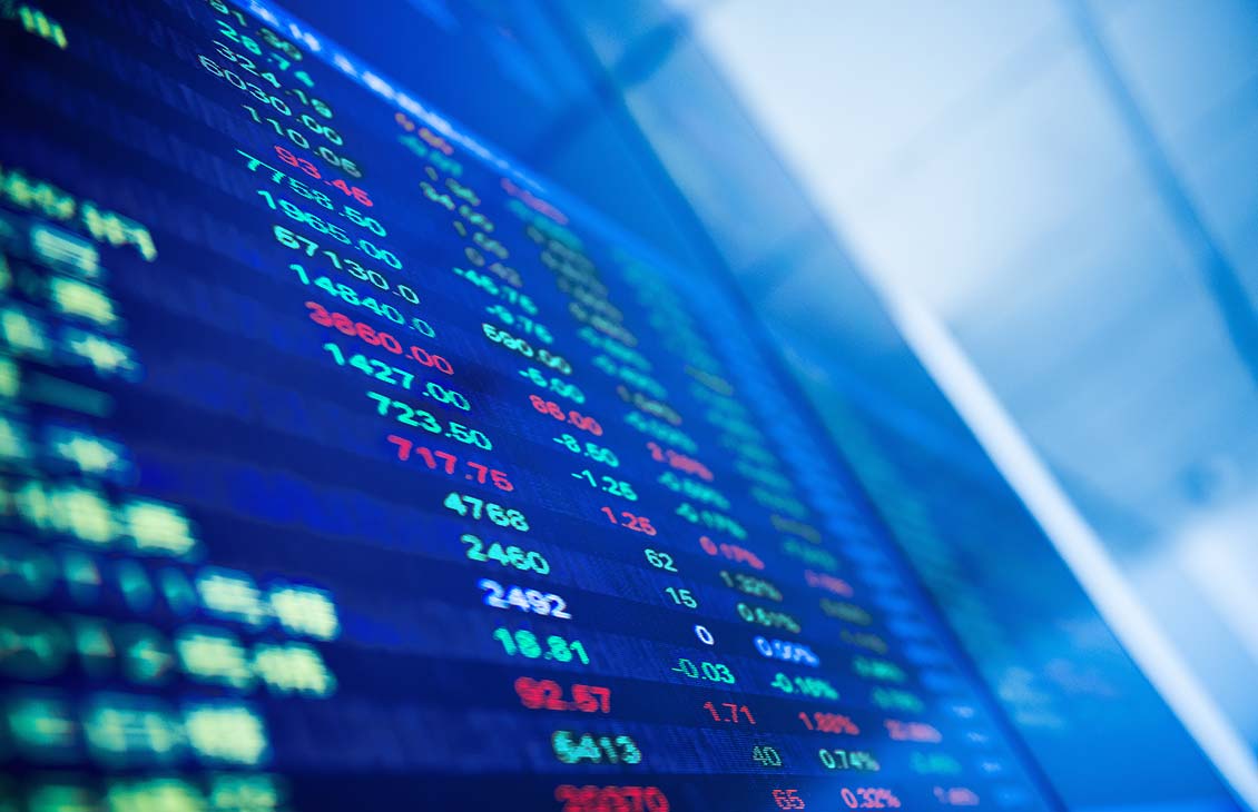 Close-up of a digital stock market board displaying rows of numbers in green, red, and blue, indicating share prices and changes against a blurred blue background.