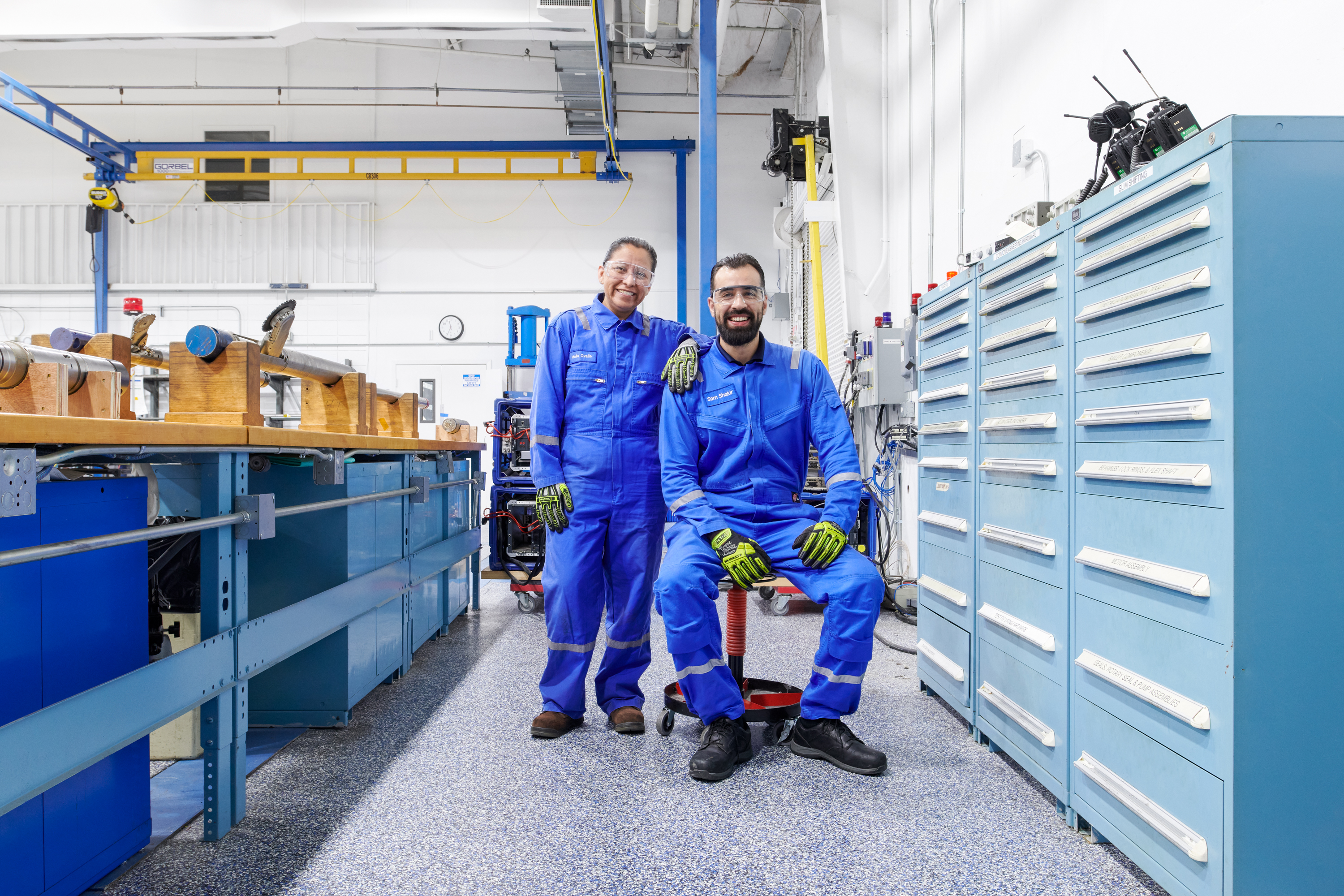 Two male SLB employees facing the camera in blue coveralls, with one sitting down and one standing.