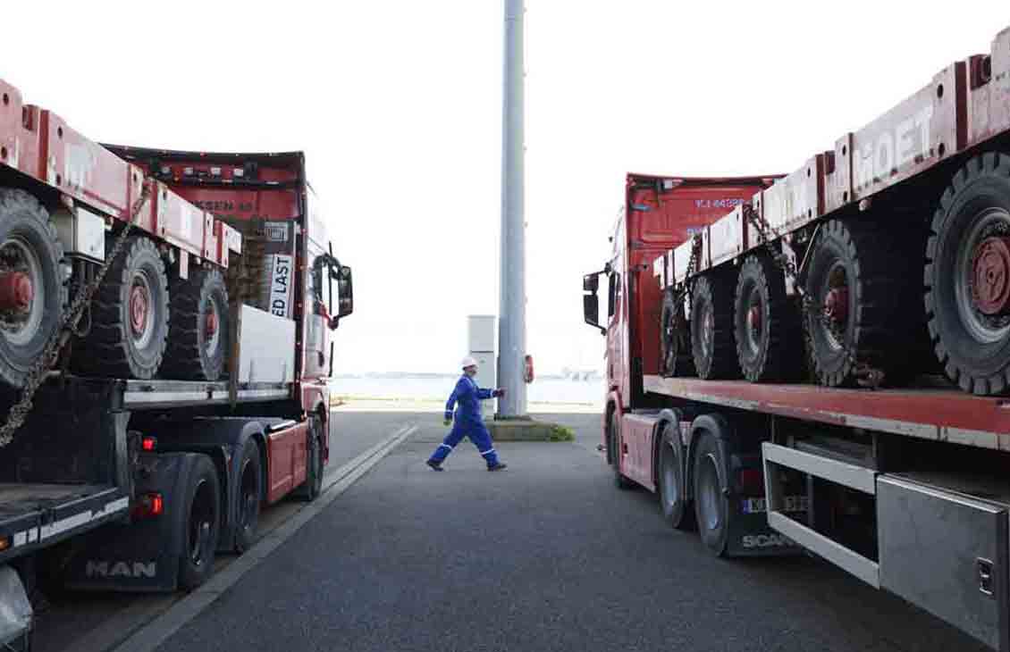 Photo of person walking, large trucks with wheeled platforms on either side