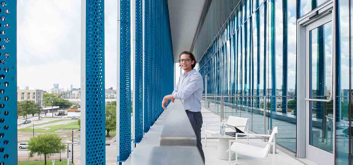 Man standing on balcony of a blue and white office building (Tier 1_Office_Houston_AML_4462)