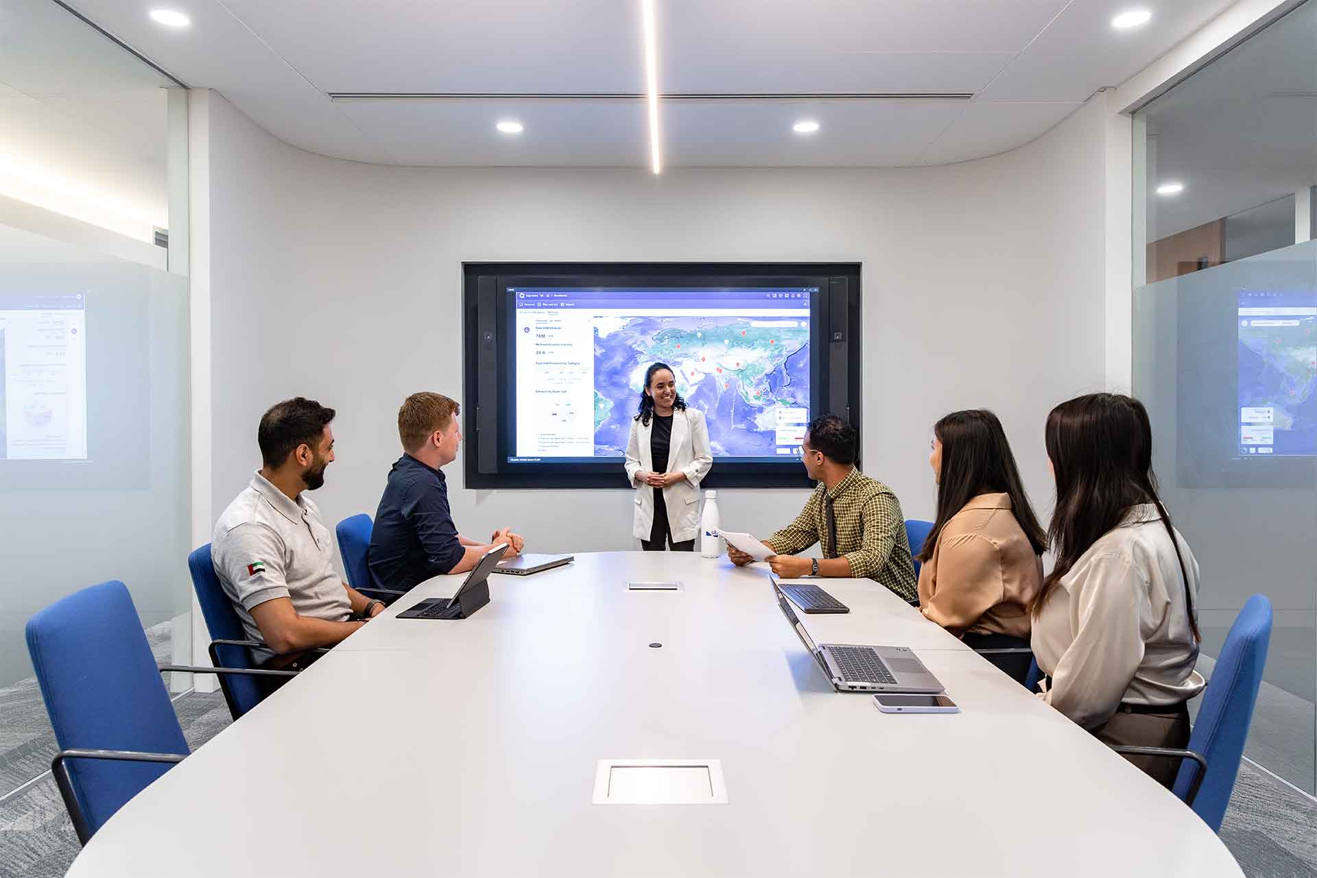 Group a people in a meeting room with a presentation screen behind the presenter