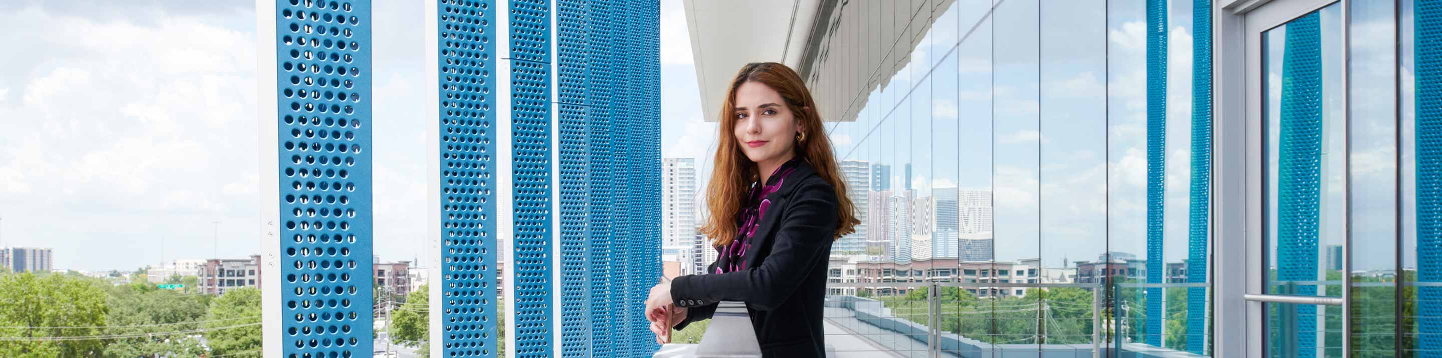 Woman standing on the balcony of a blue and white office building (Tier 1_Office_Houston_AML_4697)