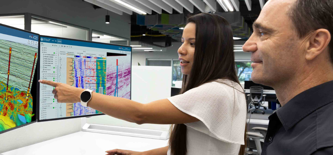 Two employees reviewing data across two computer screens