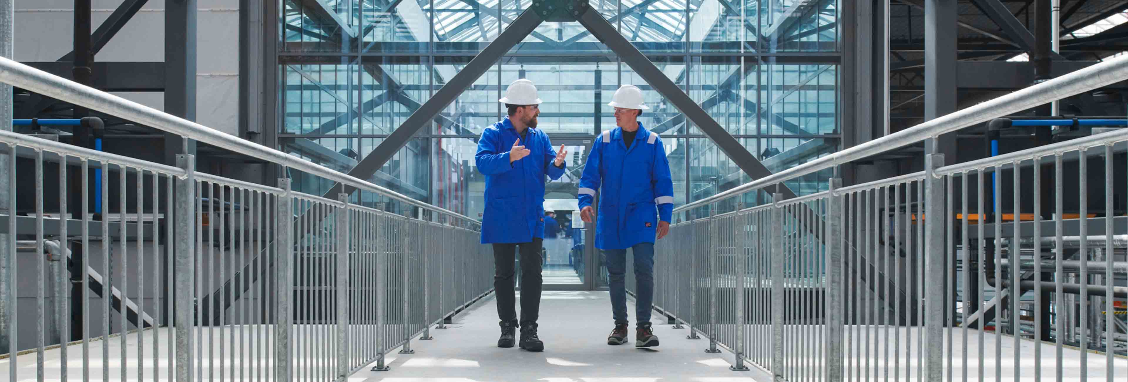 Two SLB employees with blue labcoats talking to each other while walking along a hallway