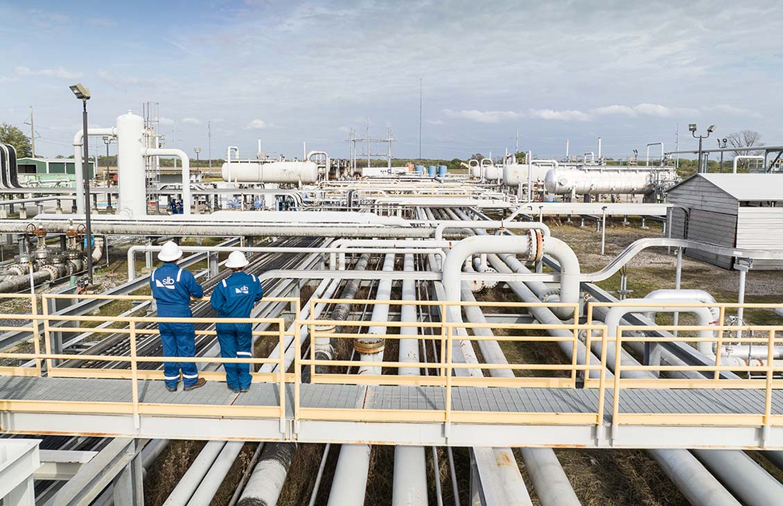Two SLB employees on a gantry overlooking a processing facility.