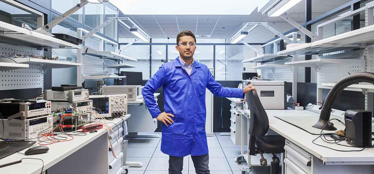 Man in blue lab coat in safety glasses posing in lab