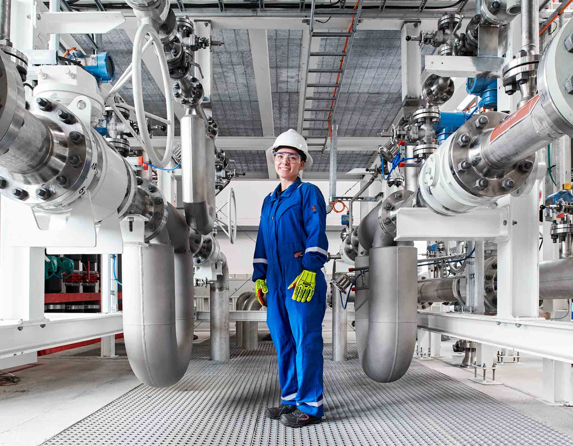 Woman in blue coveralls and safety wear checking large pipes