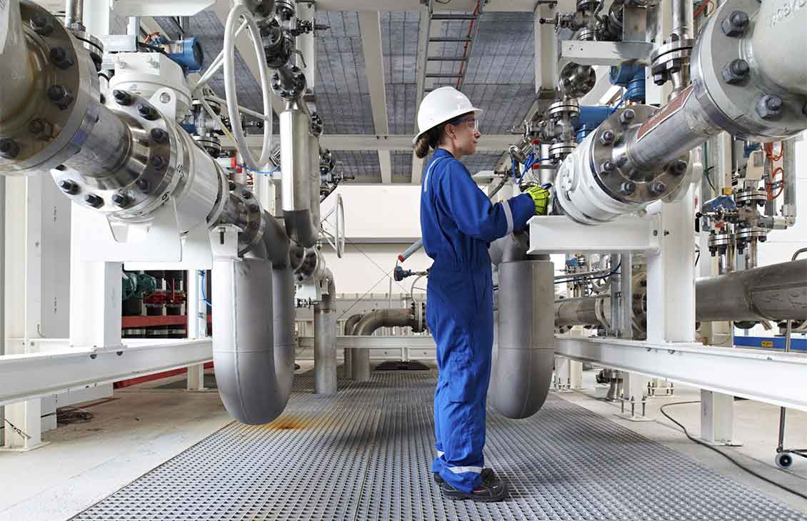 Woman in blue coveralls and safety wear checking large pipes