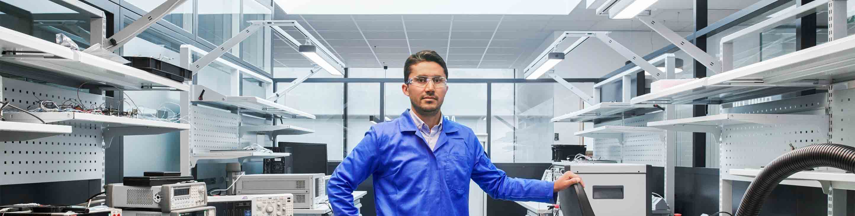 Man in blue lab coat in safety glasses posing in lab