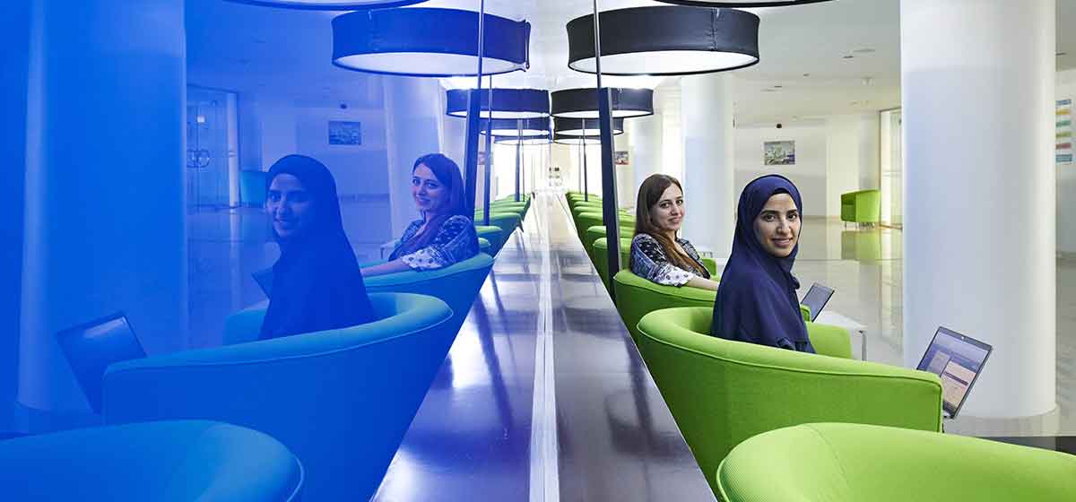 2 women, one with brown hair, the other with navy hijab sitting in green chairs with laptops on their laps. Mirror image of them on left.