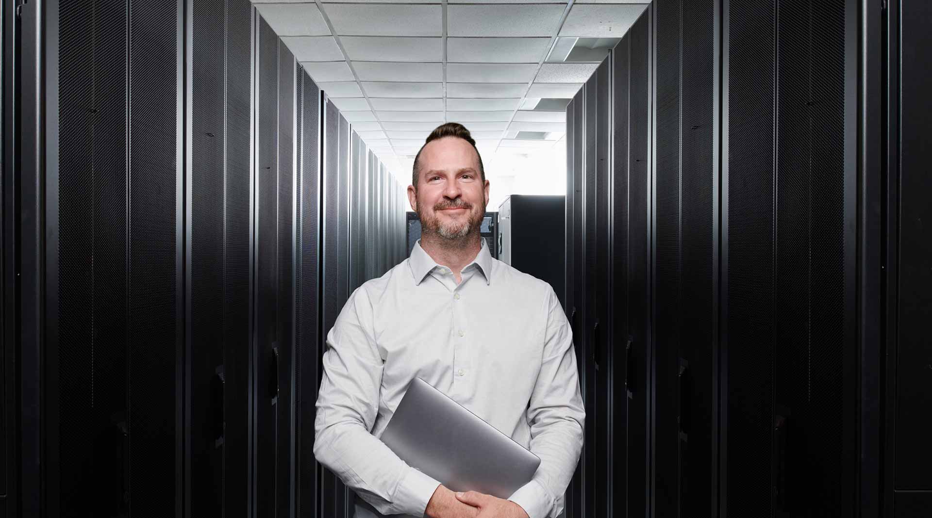 Man holding a laptop in a hallway of servers