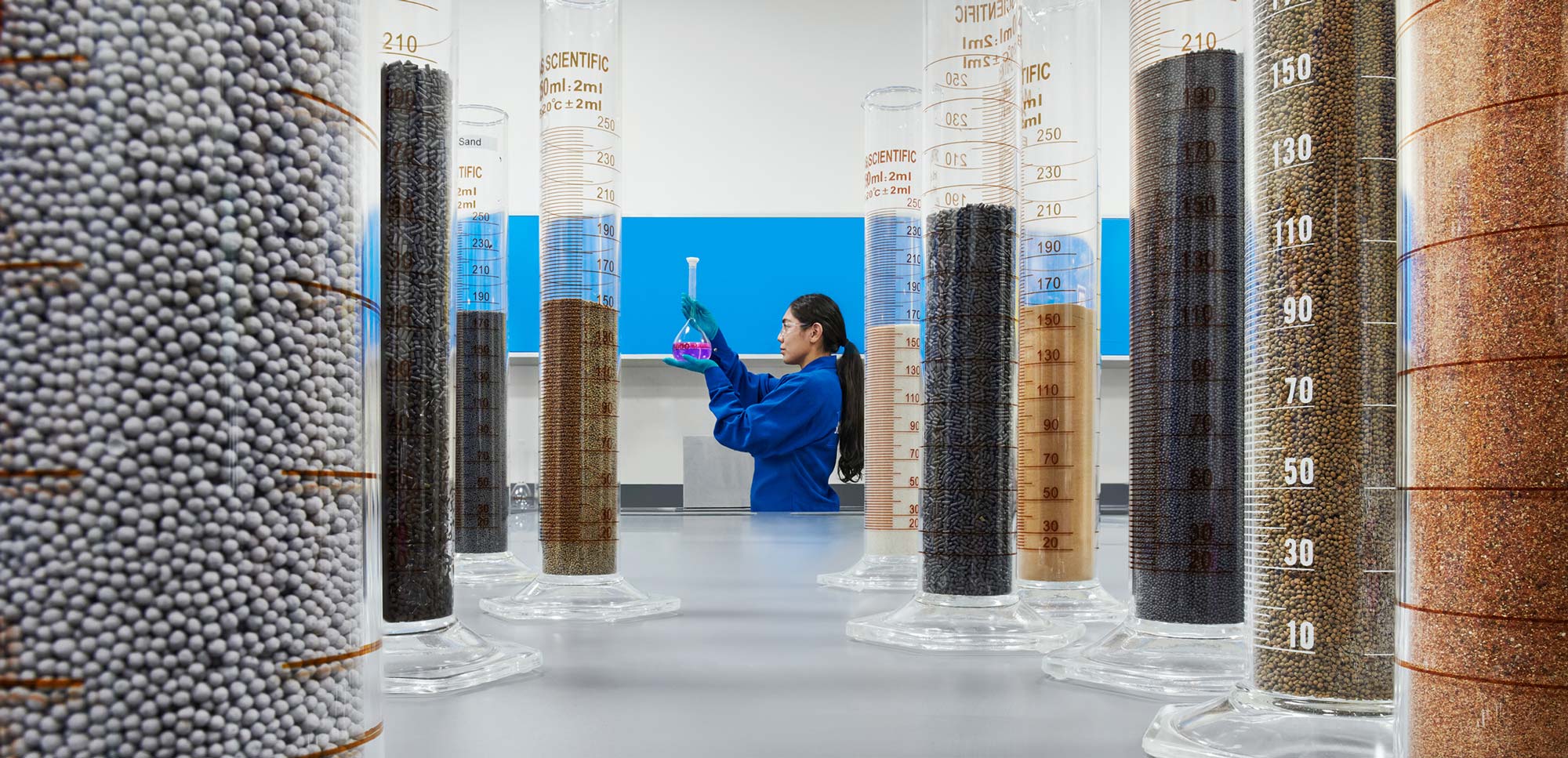 Female engineering looking at beakers with solid samples in a Learning Center, Abu Dhabi