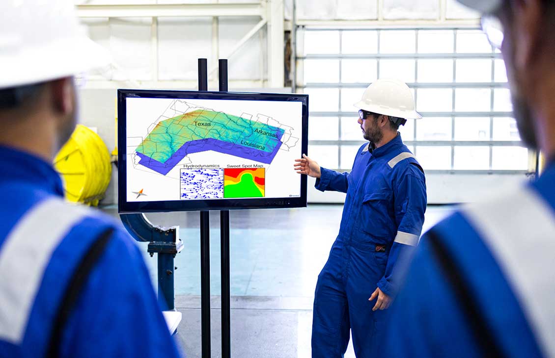 Worker in hard hat presenting subsurface map of Texas, Louisiana, and Arkansas on screen.