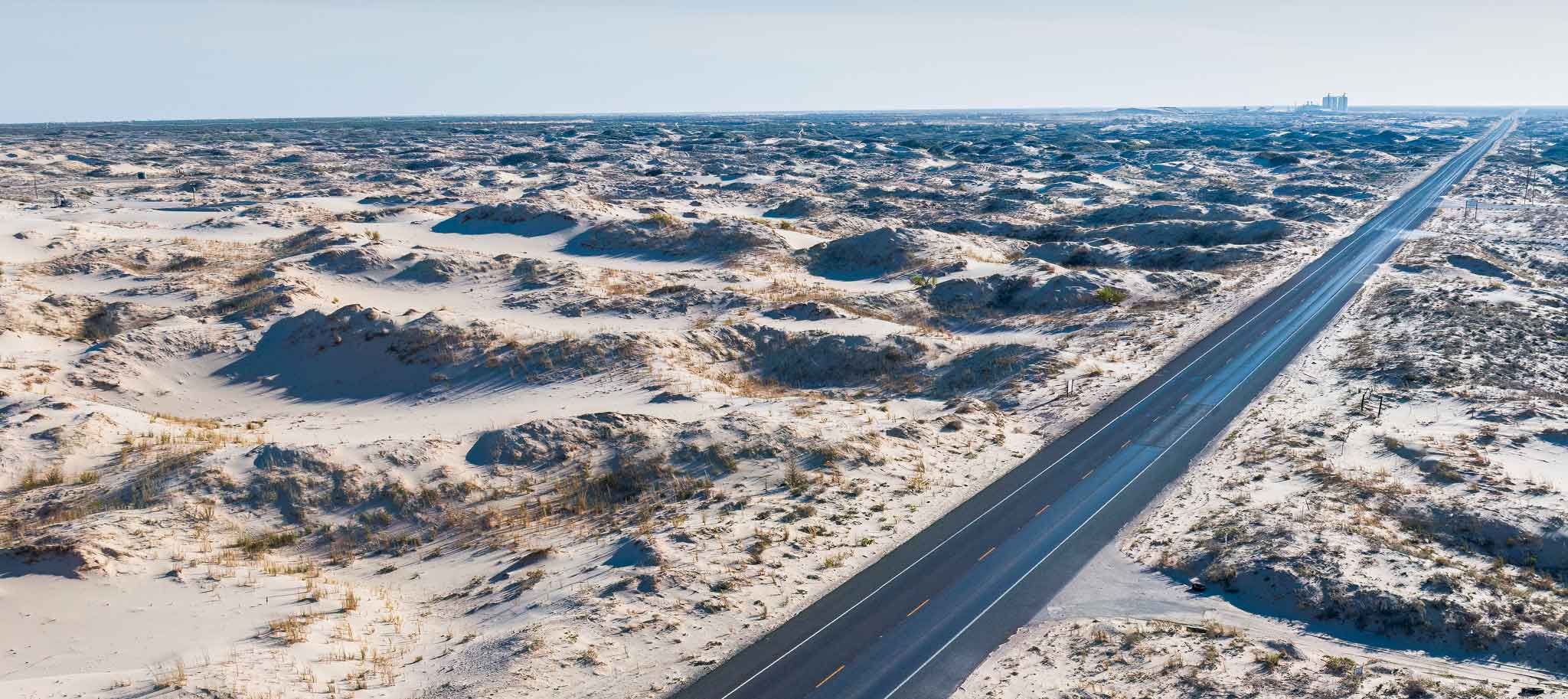 long straight road surrounded by sand dunes
