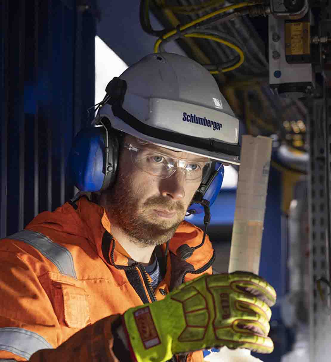 M-I SWACO employee in orange PPE looking at vial with liquid inside.